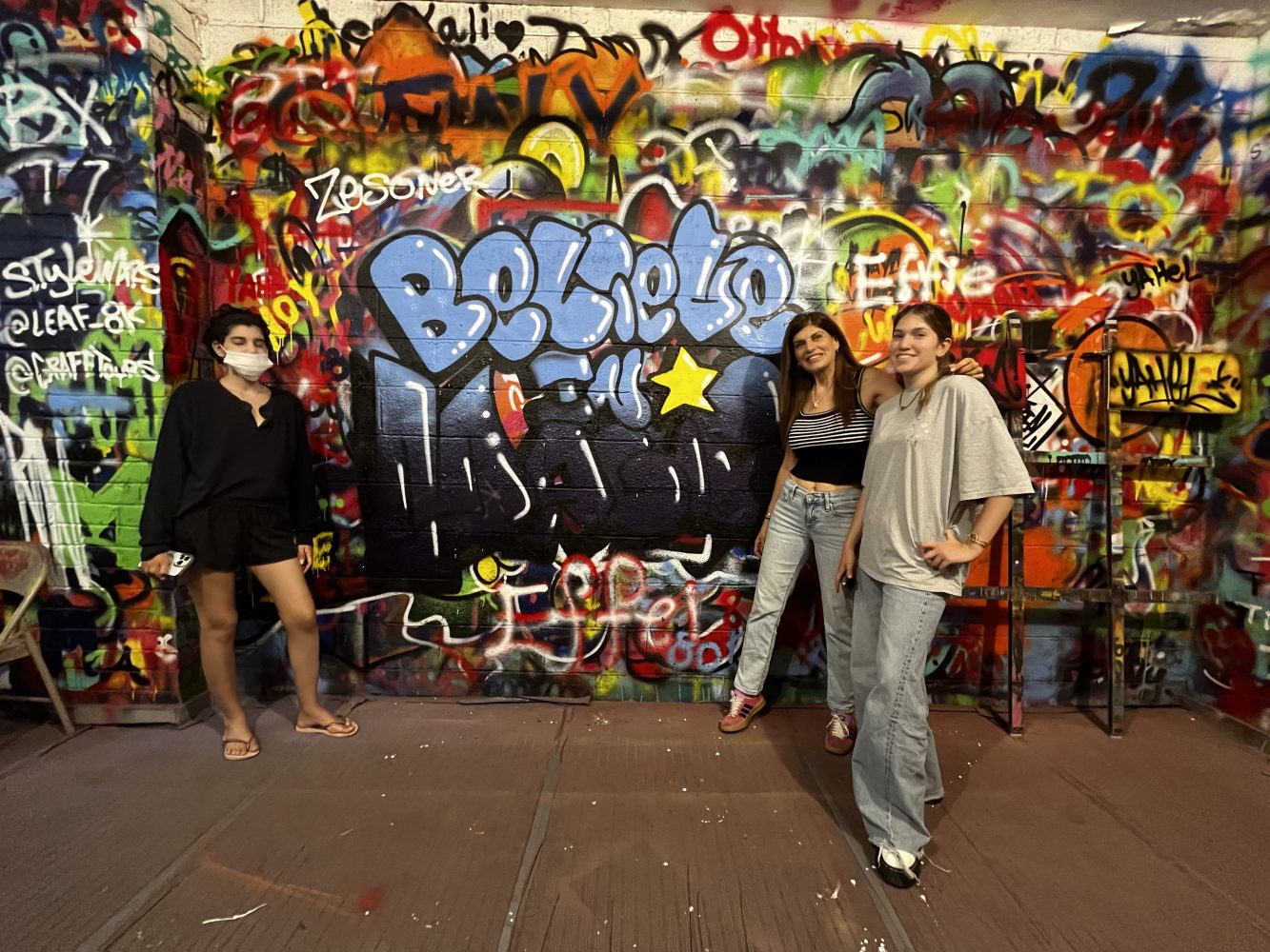 a group of people standing next to a graffiti covered wall