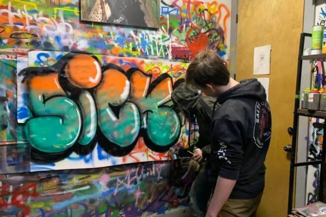 a person standing in front of a store filled with lots of colorful graffiti